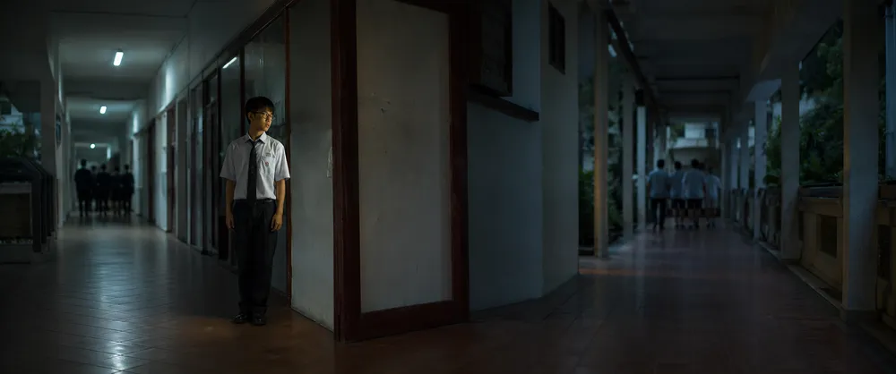 A student stands rigidly still in an empty corridor while others walk away
